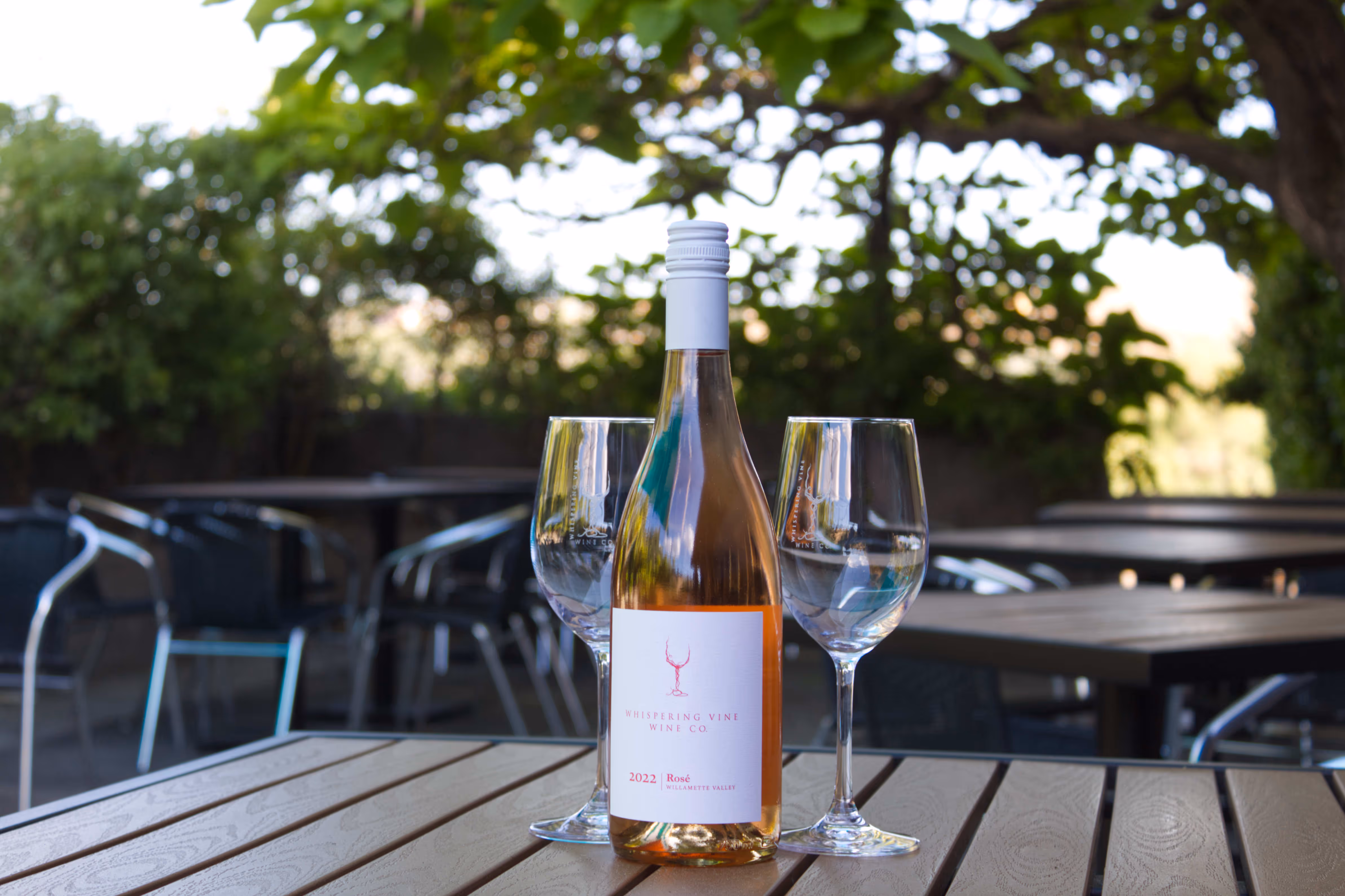 A chilled bottle of rosé and wine glasses on a sunny patio table